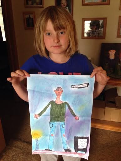 A young girl holds up a crayon drawing of a man